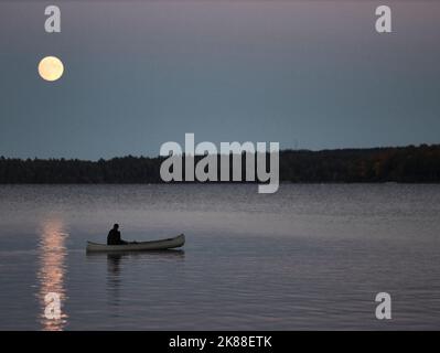 Solitario canoa pagaia sotto una luna piena sul lago Sebec nel Maine Foto Stock