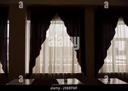 Tende nella sala da pranzo. Un sacco di tavoli. Luce dalle grandi finestre. Banchi in fila. Foto Stock