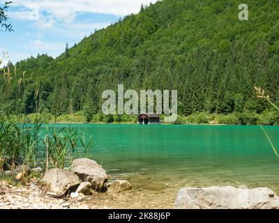 Fisher barca casa e capanna di legno con molo sulla riva del lago Walchensee below Fischberg montagna. Foto Stock