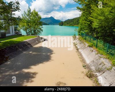 Affluente fluviale fangoso dalle vette delle Alpi dolomitiche dopo forti piogge. Il letto del fiume alimenta la corrente alla centrale idroelettrica e su Foto Stock