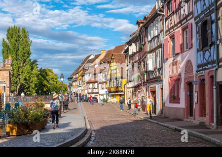 Una strada pittoresca di negozi e caffè lungo il marciapiede nel centro storico medievale di Colmar, in Francia, una delle fermate lungo la strada del vino nella zona dell'Alsazia. Foto Stock
