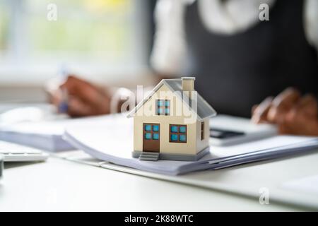 Mano della persona che fa il calcolo dell'imposta di proprietà usando il calcolatore del modello della casa Foto Stock