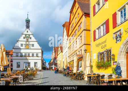 La Torre dell'Orologio di Ratstrinkstube, con negozi colorati e caffetterie sul marciapiede, si trova nella storica piazza del Municipio di Rothenburg ob der Tauber, Germania. Foto Stock