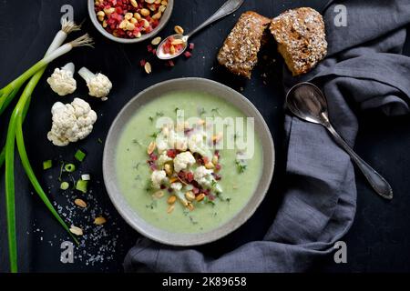 Zuppa cremosa di cavolfiore con cipolline, rafano, arachidi e prosciutto a dadini, servita con un rotolo integrale Foto Stock