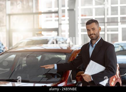 Giovane consulente maschile che mostra la nuova auto in auto show. Concetto per il noleggio auto Foto Stock