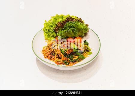 Spaghetti piccanti con verdure e pancetta croccante su piatto bianco. Foto Stock