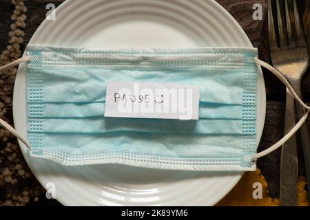 la parola pausa su carta si trova su una maschera medica in una piastra sul tavolo, quarantena auto-isolamento, riposo, assistenza sanitaria e maschera medica Foto Stock