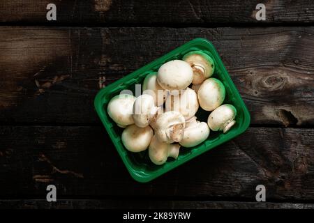 funghi champignons in una scatola di plastica blu su un vecchio tavolo di legno in cucina, curvature grezze dal negozio Foto Stock