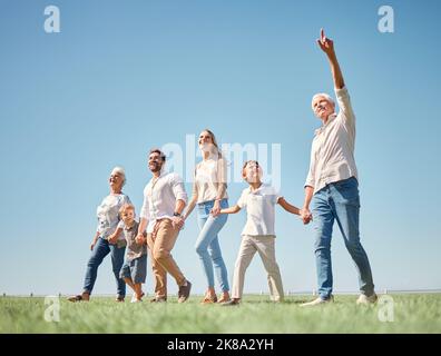 Famiglia, passeggiata e natura insieme al campo, erba e sole durante la vacanza. Mamma, papà e bambini camminano in boschi verdi o parco in primavera Foto Stock