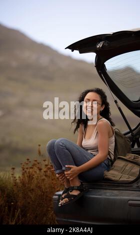 Un viaggio su strada non riguarda la destinazione, ma il viaggio, una giovane donna seduta su un'auto mentre si ferma durante un viaggio su strada. Foto Stock