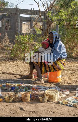 Tarangire, Tanzania - 12th ottobre 2022: Una donna Masai che tiene un bambino mentre vende i monili e gli ornamenti fatti a mano su una strada all'alba. Foto Stock