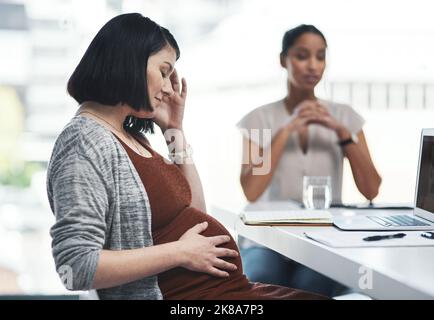 Potrebbe essere il momento di ridurre le mie ore: Una giovane donna d'affari incinta si sente stressata durante una riunione di squadra in un ufficio moderno. Foto Stock