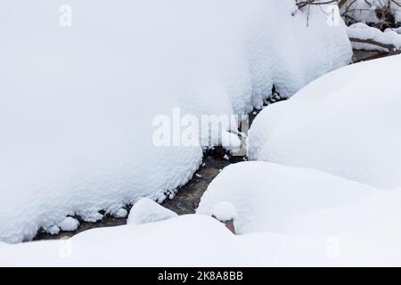 Un ruscello che scorre tra un grande strato di neve in inverno Foto Stock