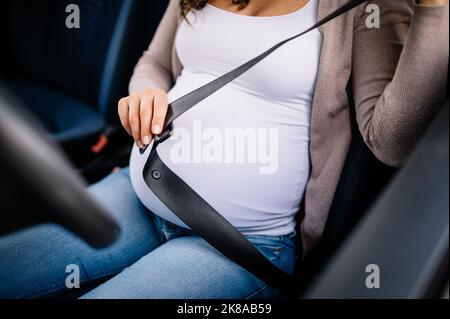 Primo piano di una donna incinta seduta in auto e allacciare la cintura di sicurezza Foto Stock