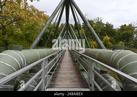 Due condutture metalliche dipinte di verde in prospettiva ridotta su entrambi i lati del ponte di lavoro in legno che attraversa il fiume. Foto Stock