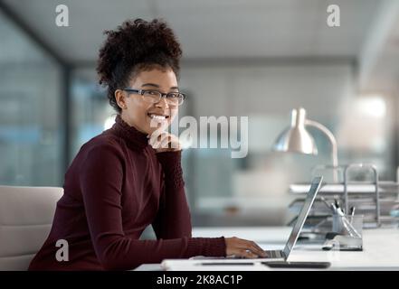 Il vostro successo e la vostra felicità stanno in voi. Una giovane donna d'affari sicura che lavora in un ufficio moderno con la sua mano sul suo mento sorridente. Foto Stock