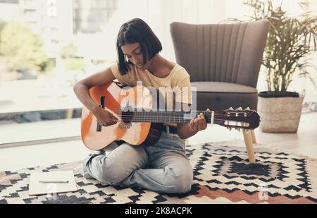 Qualunque cosa accada nel mondo, la musica mantiene un ritmo costante. Una giovane donna suona la chitarra a casa. Foto Stock