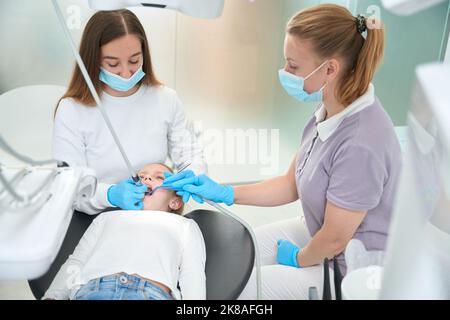 Pedodontist che tratta la carie dentaria in bambina preseen assistita da infermiera Foto Stock