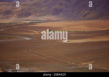 Vista aerea dall'alto strada che taglia attraverso il paesaggio grafico arido deserto freddo montagne aride che contrastano campi verdi fattorie nella valle del fiume Foto Stock