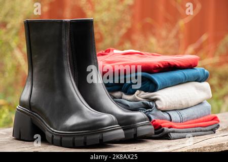 stivali neri alti da donna con suole spesse e un mucchio di cose si levano in piedi su un asse di legno al sole sulla strada, scarpe da donna e abiti invernali, fas Foto Stock