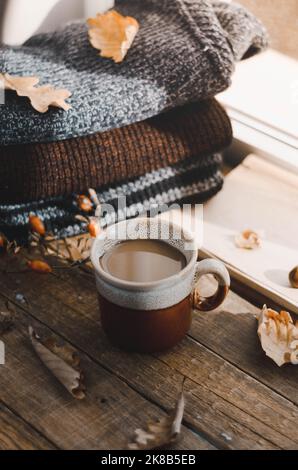 Tazza grande di cappuccino su sfondo marrone vintage. Autunno, foglie autunnali, tazza di caffè calda e fumante e una sciarpa calda su sfondo tavolo di legno. Mari Foto Stock