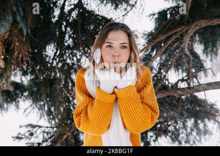 Teen bionda in un maglione giallo fuori in inverno. Una ragazza adolescente in una passeggiata in abiti invernali in una foresta innevata. Foto Stock