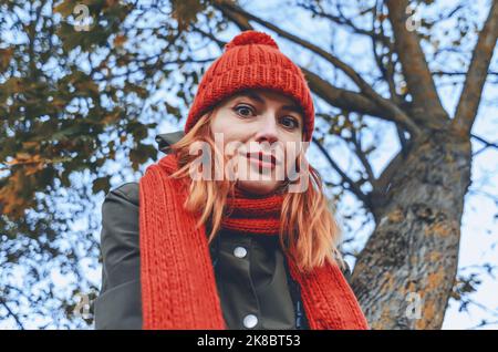 Giovane donna sorridente carina in un caldo cappello a maglia arancione e sciarpa. Primo piano ritratto autunnale. Sfondo sfocato Foto Stock