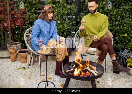 Giovane coppia che trascorre il tempo a cena accanto al fuoco sul cortile Foto Stock