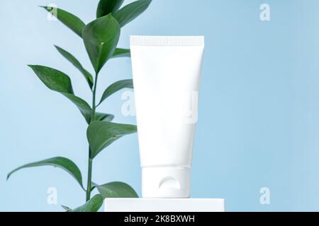 Tubo bianco bianco crema cosmetica per mock up sul podio bianco su sfondo blu. Confezione di prodotti di bellezza Foto Stock