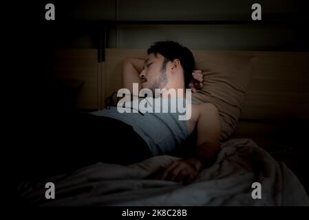 Bel giovane uomo asiatico che dorme cozily su un letto nella sua camera da letto di notte. Foto Stock