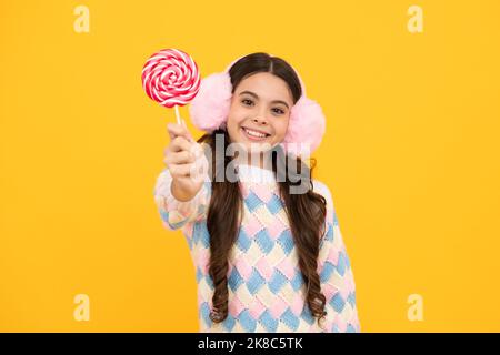 Bambino teen freddo con lollipop sopra sfondo isolato giallo. Dolce vita d'infanzia. Ragazza teen con caramella lollipop yummy. Foto Stock