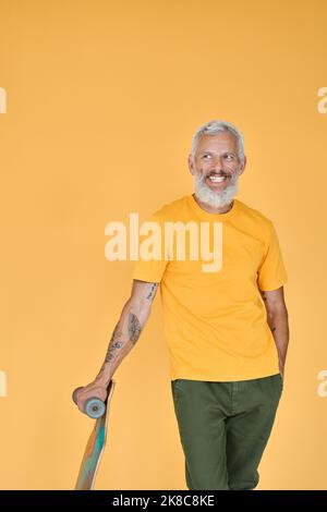 Felice fresco vecchio skater senior con skateboard isolato sul giallo. Foto Stock