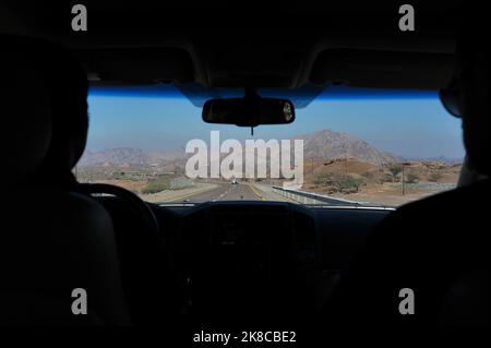 Giorno estivo vista in auto della strada, montagne rocciose, cielo blu. Prospettiva dall'interno dell'auto in movimento. Conducente, passeggero del sedile anteriore, plancia nella silhouette. Foto Stock