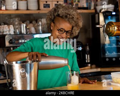 Cameriera felice afro-americana che serve un cocktail o un drink in un pub. Foto Stock