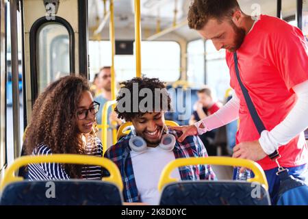 Un piccolo gruppo di amici multiculturali che guardano il tablet mentre si guida sull'autobus cittadino. Foto Stock