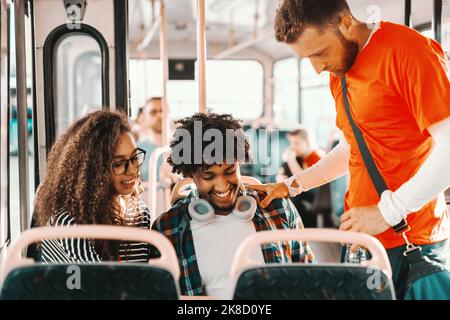 Un piccolo gruppo di amici multiculturali che guardano il tablet mentre si guida sull'autobus cittadino. Foto Stock