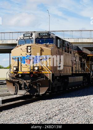 Davanti alla potente locomotiva diesel della Union Pacific che tira un lungo treno per auto da trasporto sotto un cavalcavia stradale cittadino. Foto Stock