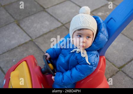 cute toddler sta guidando il suo scooter giocattolo e spingere l'automobile nel cortile posteriore Foto Stock