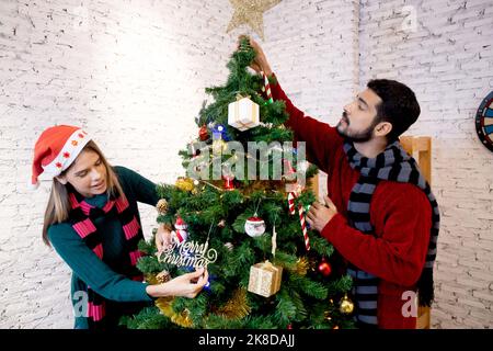 Felice giovane coppia decorazione e preparazione ornamento su albero di Natale insieme a godere a casa, uomo e donna decorazione festa natale con exci Foto Stock
