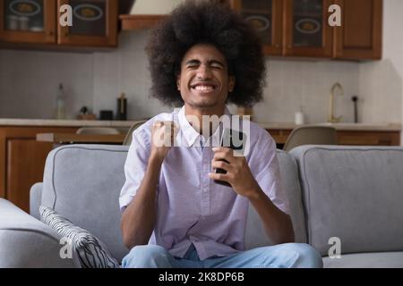 African Guy tiene smartphone si sente gioioso celebrare grandi notizie sms Foto Stock