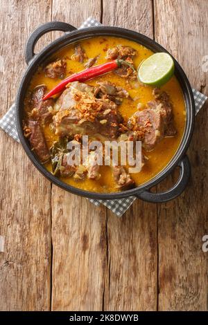 Curry piccante di capra con latte di cocco e spezie in primo piano in una padella sul tavolo. Vista verticale dall'alto Foto Stock