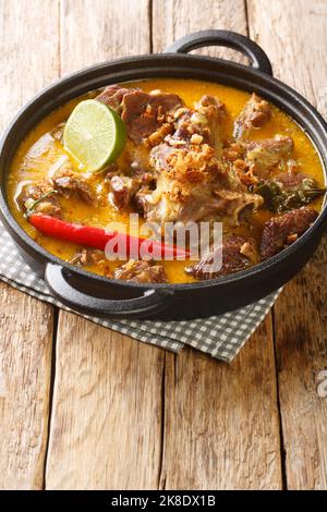 Curry piccante di capra con latte di cocco e spezie in primo piano in una padella sul tavolo. Verticale Foto Stock