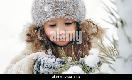 Decorazione esterna dell'albero di Natale. cutie, bambina graziosa decora l'albero di Natale innevato con giocattoli di ghiaccio fatti in casa, durante le nevicate, nella foresta. Happy time nelle nevose giornate invernali. Attività invernali in famiglia all'aperto. Slow motion. Foto di alta qualità Foto Stock