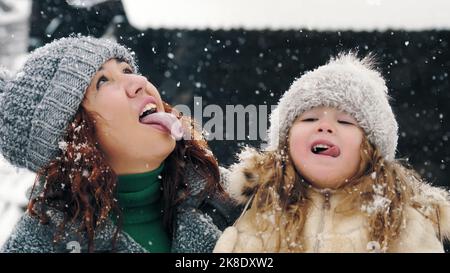 divertimento invernale per tutta la famiglia. cattura i fiocchi di neve con la lingua. Famiglia felice, madre e figlia stanno interferendo i fiocchi di neve con le loro lingue, godendosi della neve e della caduta di neve, avendo divertimento, spendendo insieme il tempo in giorno di inverno nevoso. Slow motion. Foto di alta qualità Foto Stock