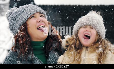 divertimento invernale per tutta la famiglia. cattura i fiocchi di neve con la lingua. Famiglia felice, madre e figlia stanno interferendo i fiocchi di neve con le loro lingue, godendosi della neve e della caduta di neve, avendo divertimento, spendendo insieme il tempo in giorno di inverno nevoso. Slow motion. Foto di alta qualità Foto Stock