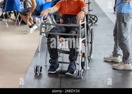 Ragazzo con problemi di mobilità negli arti inferiori seduto in una sua sedia a rotelle Pronto a stare in piedi verticale grazie a un esoscheletro meccanico. Foto Stock