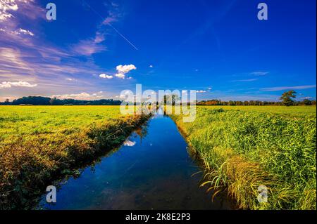 Un piccolo canale di irrigazione tra due campi con riflesso di nuvole e il cielo blu in autunno, Hagenburg, bassa Sassonia, Germania Foto Stock