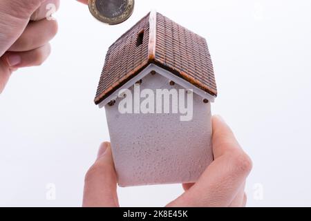 Mano moneta caduta nel salvadanaio a forma di un modello di casa Foto Stock