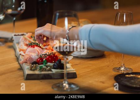 Mano femmina che prende una mandorla da un piatto di legno con prosciutto, formaggio, prugne, noci e pomodori ciliegini servito accompagnamento, colpo da primo piano. Foto Stock