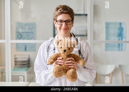 Ritratto di pediatra femminile in occhiali che tengono il giocattolo e guardando la fotocamera mentre si è in ufficio Foto Stock